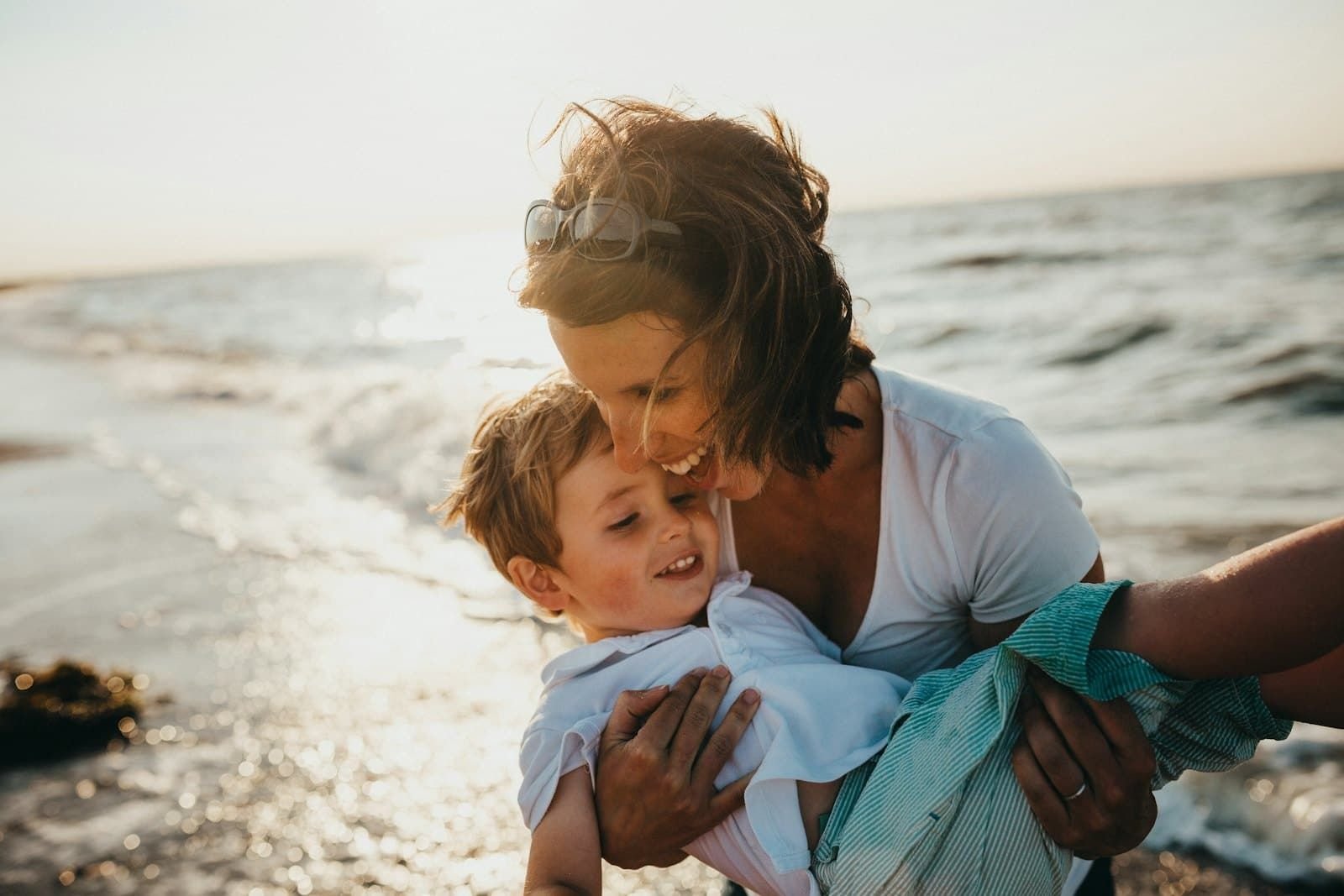 Mutter mit Kleinkind am Strand im warmen Licht.